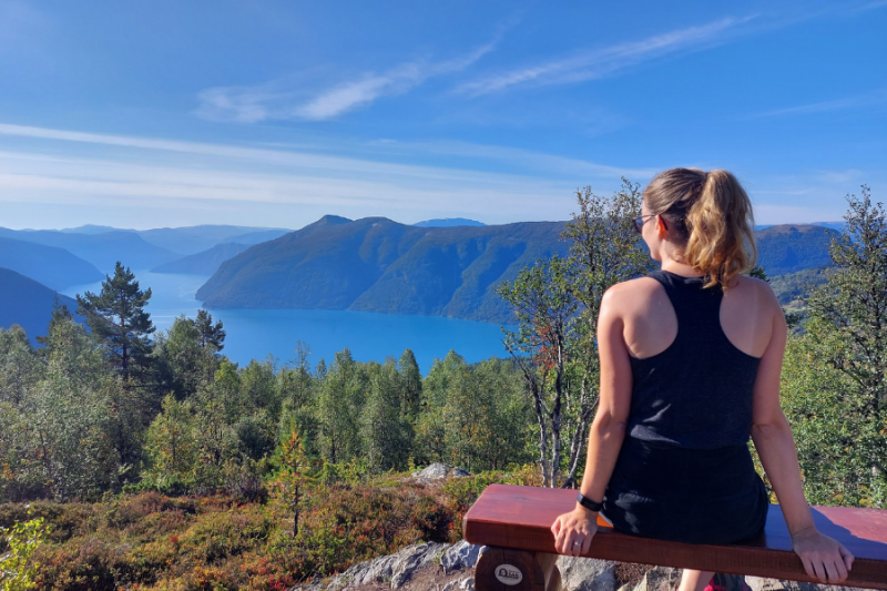 Zittend op een bankje op de top van Mount Molden met uitzicht over helderblauw water in de fjord.