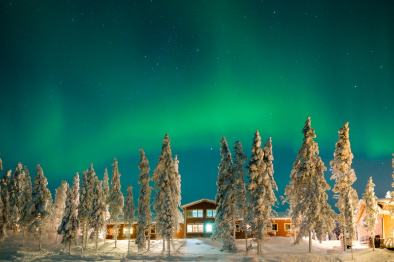 Het groene noorderlicht boven een lodge in de verte in Lapland.