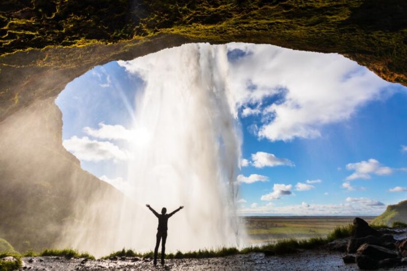 Persoon staat achter de Seljalandsfoss waterval in IJsland met Nordic, de Scandinaviëspecialist